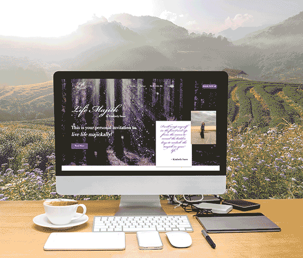 Life Majick website displayed on a desktop computer, surrounded by a coffee cup, notebooks, and natural outdoor elements in the background.