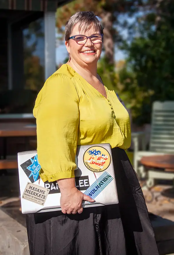 Jackie Barker, spiritual website designer and digital marketer, smiling with confidence while holding a sticker-covered laptop. She stands outdoors in natural light, embodying her creative and soulful approach to branding, web design, and marketing.