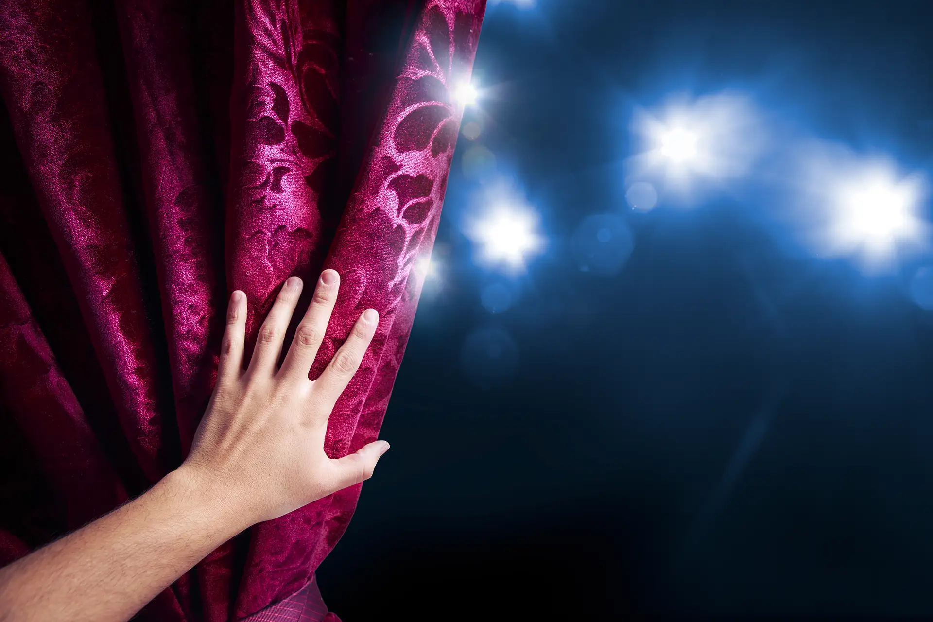 Hand pulling theater curtain under spotlight, spiritual stage set