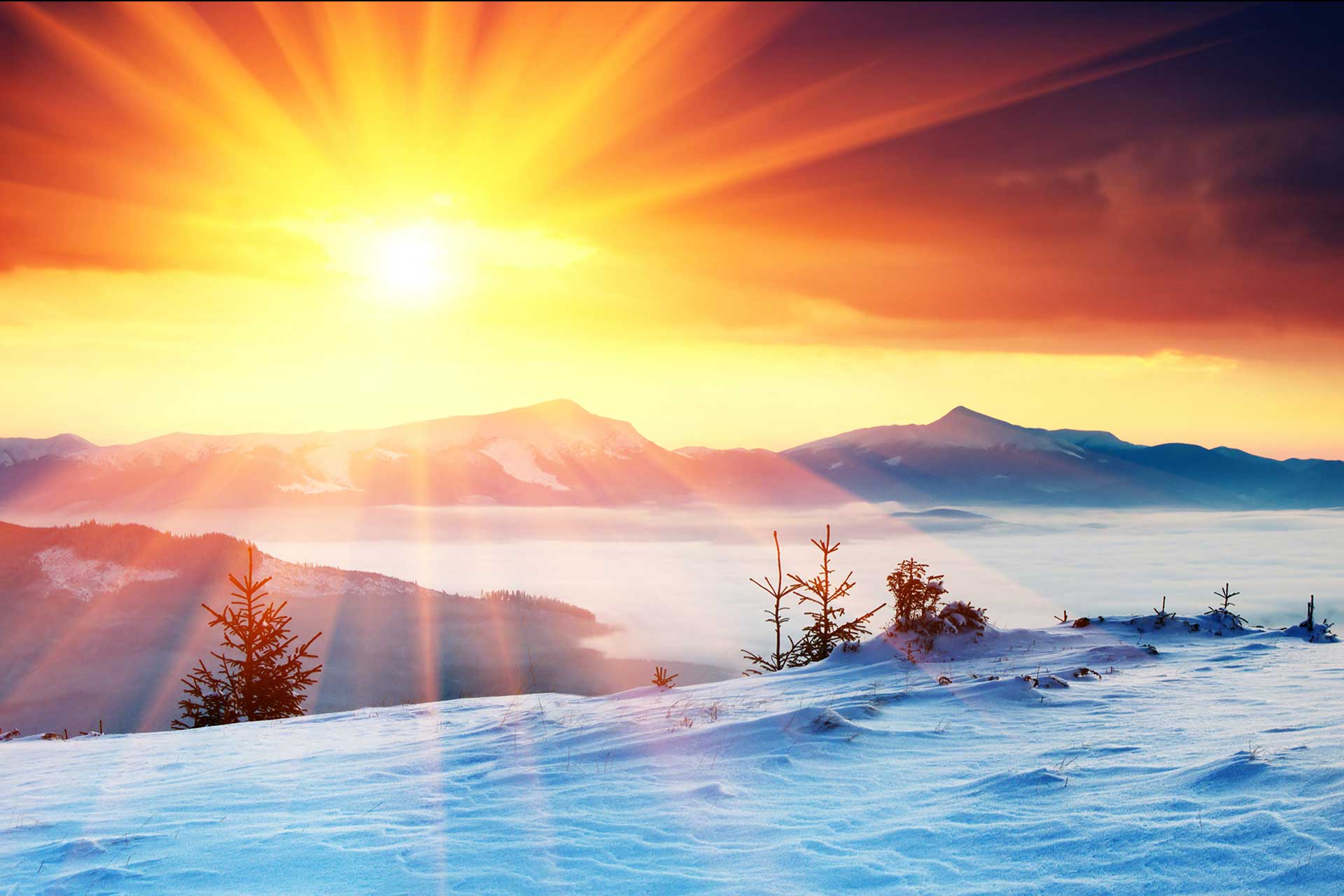 Sunrise over a snowy mountain landscape, with rays of light piercing through the clouds onto the frost-covered peaks and trees.