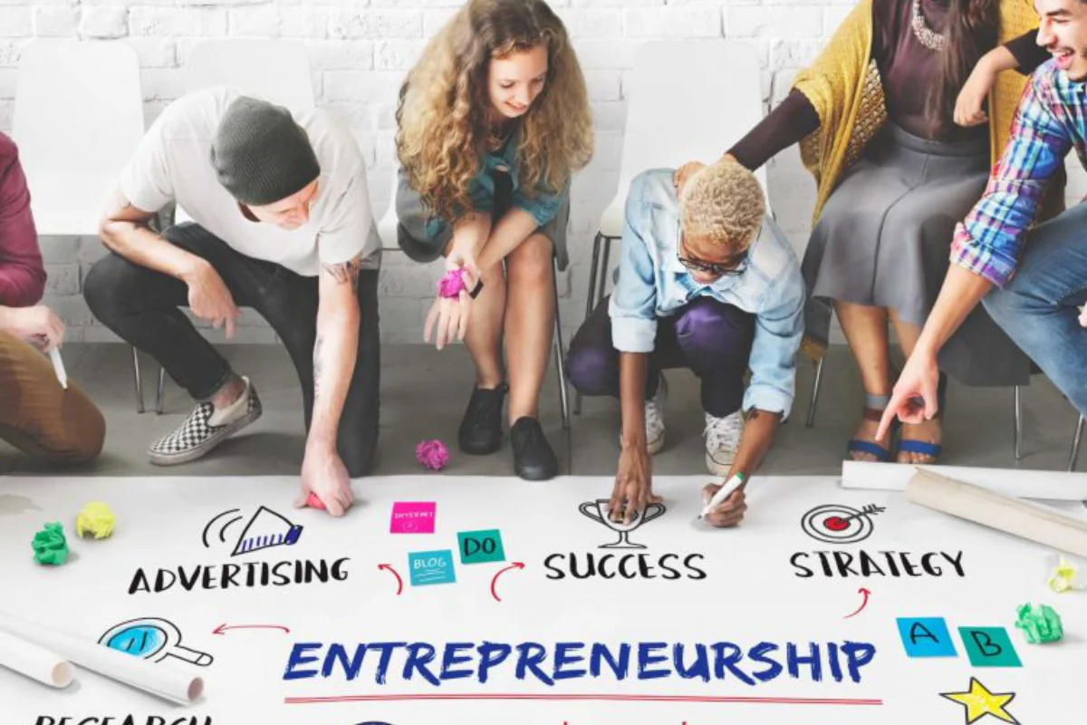 Group of young entrepreneurs collaborating on a project, with a whiteboard displaying words like advertising, success, and strategy.