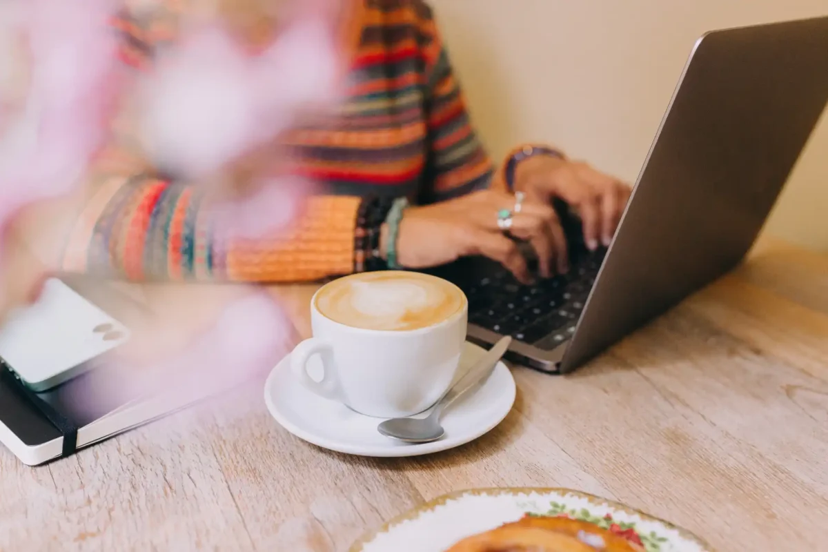 Woman typing on a laptop in a cozy café while learning about email authentication over coffee and pastry.