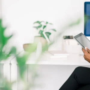 Woman sitting in a bright, plant-filled workspace using a tablet—soul aligned business in flow