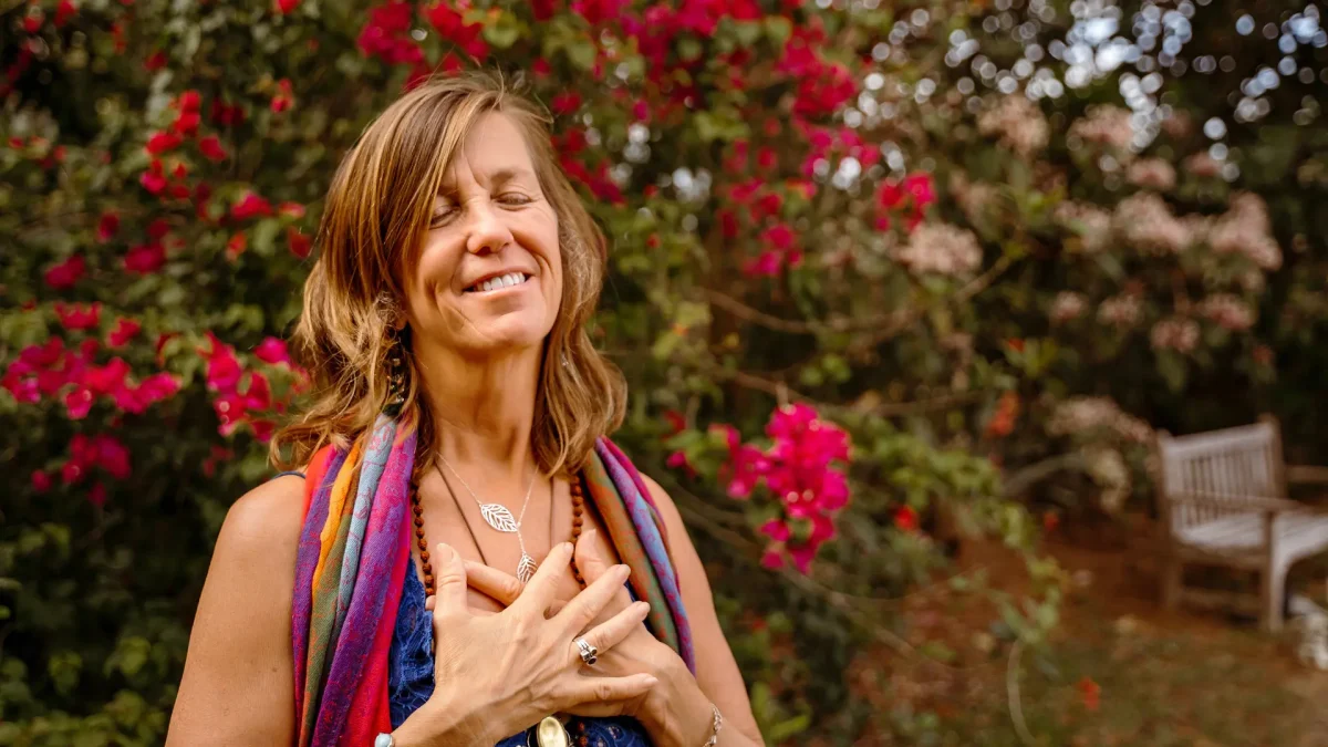 Spiritual entrepreneur standing with hands on heart, smiling with eyes closed in front of blooming pink flowers, embodying peace and clarity—symbolizing the power of soulful business alignment strategies.