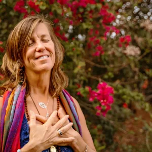 Spiritual entrepreneur standing with hands on heart, smiling with eyes closed in front of blooming pink flowers, embodying peace and clarity—symbolizing the power of soulful business alignment strategies.